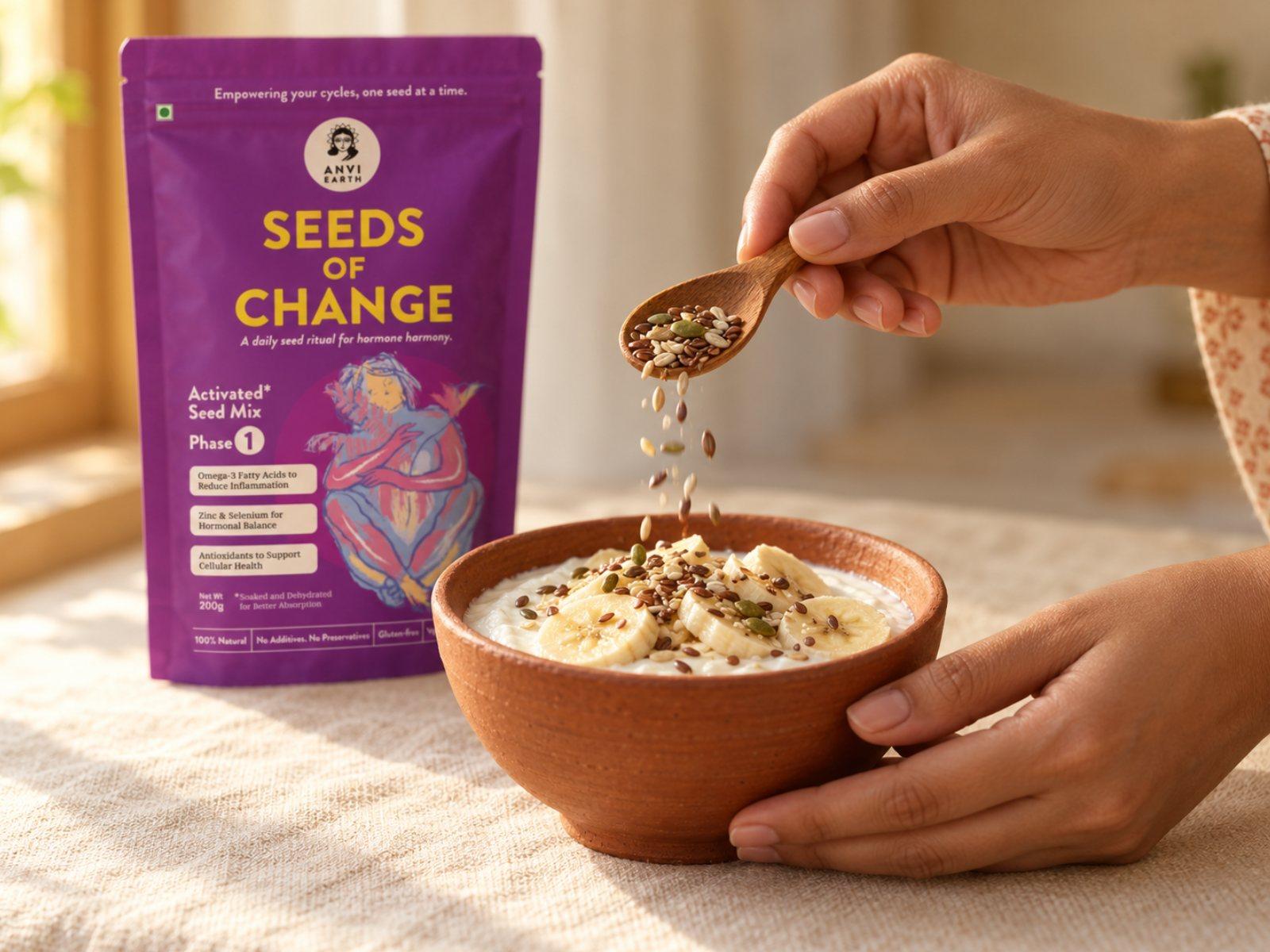 A hand sprinkling a spoonful of activated seed mix over a bowl of yoghurt, the Seeds of Change pack behind